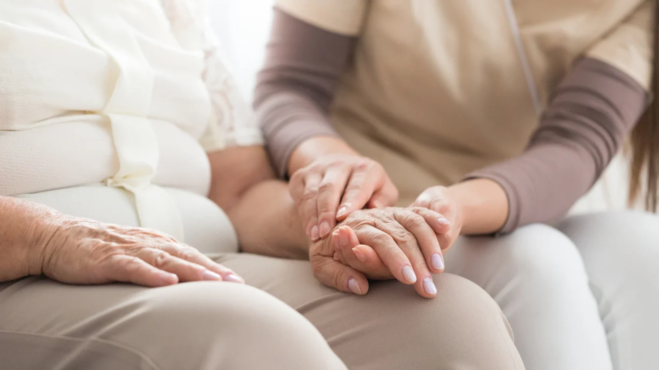Primer plano de una mujer joven cogiendo con suavidad con sus dos manos la mano izquierda de una mujer de avanzada edad