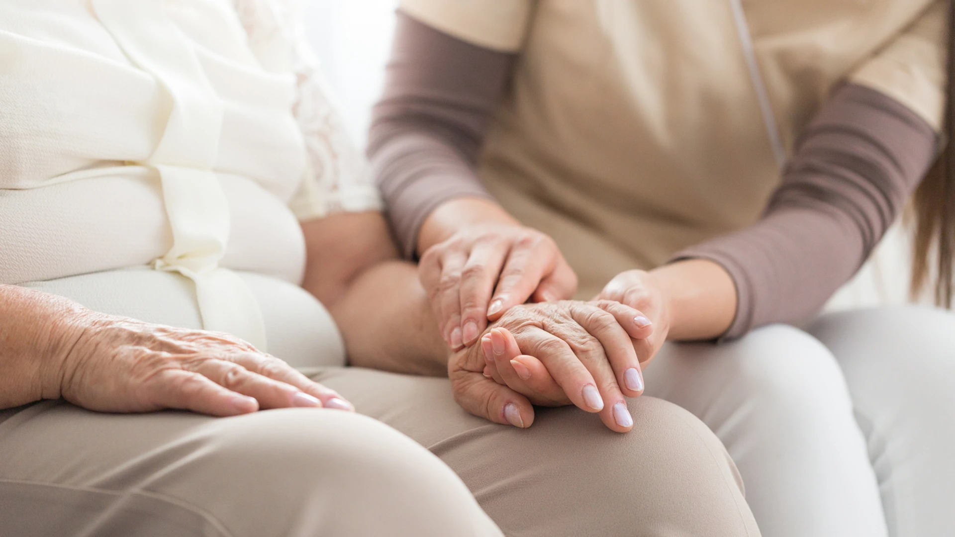 Primer plano de una mujer joven cogiendo con suavidad con sus dos manos la mano izquierda de una mujer de avanzada edad